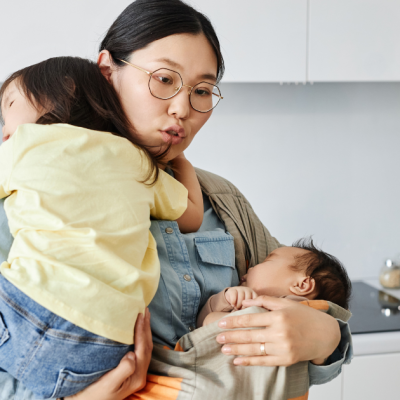 Mum holding baby and toddler at the same time in kitchen. Blog for Life Charity UK