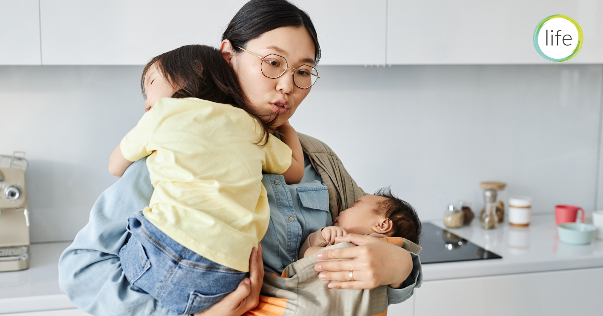 Mum holding baby and toddler at the same time in kitchen. Blog for Life Charity UK