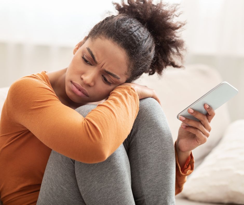 Woman sat on couch looking sad with mobile phone in hand