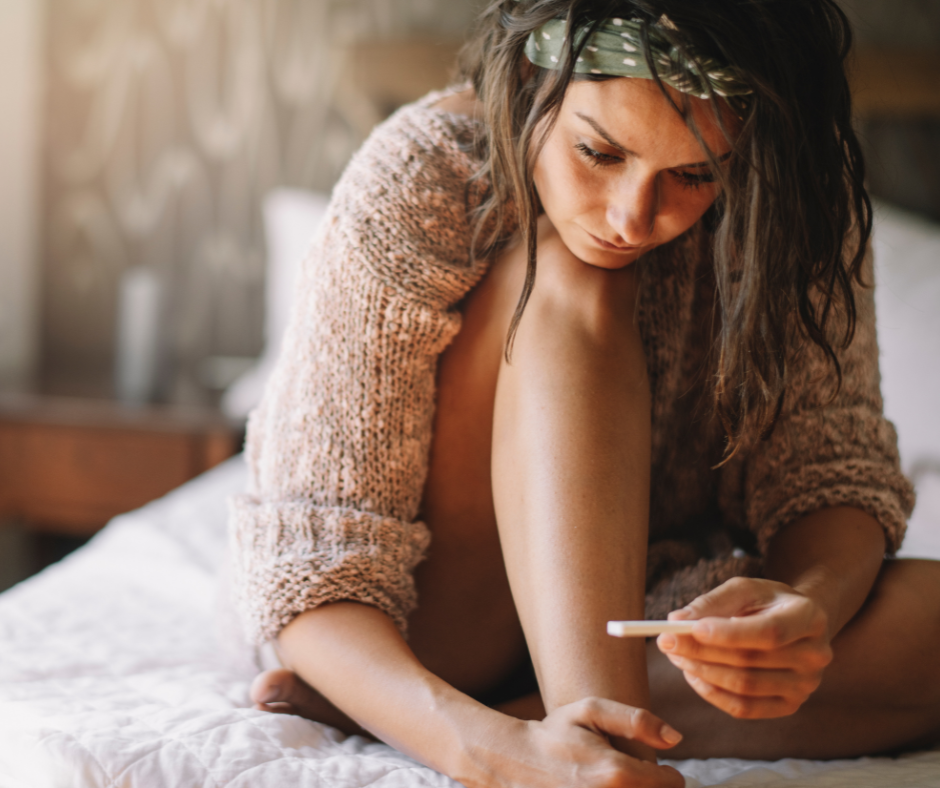 Young woman sitting on bed looking at a positive pregnancy test